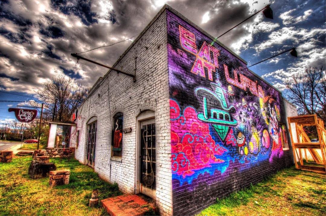 The side of the building painted with a colourful Eat At Lupie's mural, the coffee cup sign at the corner of the lot.
