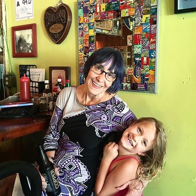 A woman and a young girl laughing together by the counter, in front of a mirror framed with soda labels.