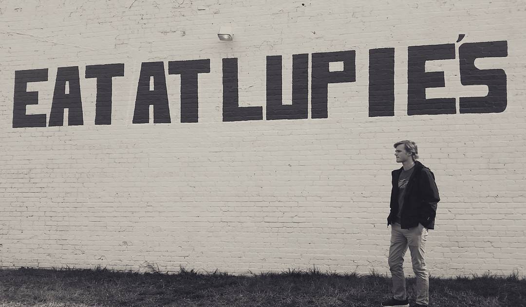 The painted brick wall beside the cafe reading Eat At Lupie's.
